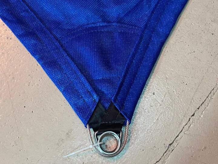 Reinforced corner of a blue shade sail with a stainless thimble and perimeter wire rope