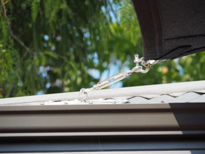 Stainless steel turnbuckle tensioning a black shade sail down to a roof fixing