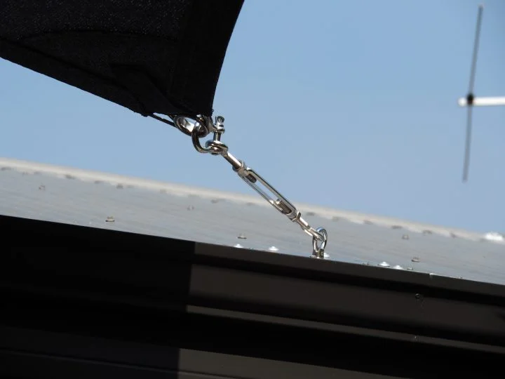 Black shade sail corner tensioned to a metal roof fixing with a stainless turnbuckle